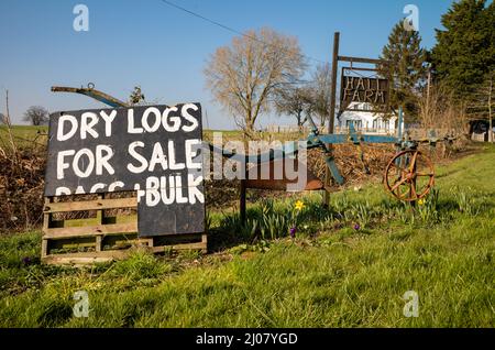 Ein alter Pflug und ein Brett, das am Eingang zur Hall Farm in Wotham, Norfolk, Großbritannien, Holzstämme zum Verkauf anbietet Stockfoto