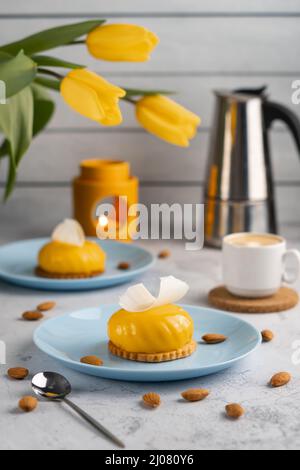 Gelbe Cupcakes und eine Tasse Kaffee mit gelben Tulpen auf betonem Hintergrund. Leckeres Dessert am Morgen Stockfoto