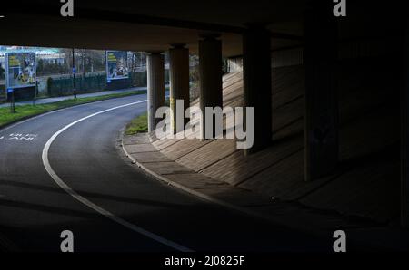 Eine leere Unterführung mit Straßenüberführung, die Stützsäulen und Straßen in Schatten und Licht zeigt. Stockfoto