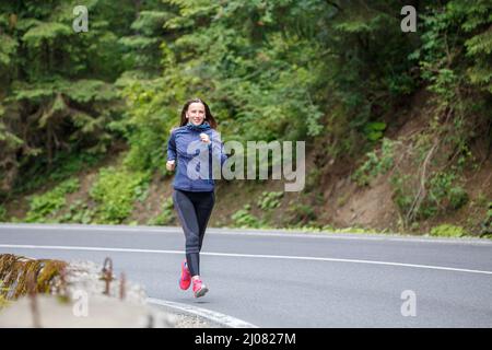 Läuferin, die auf der Bergstraße durch den Wald läuft. Stockfoto