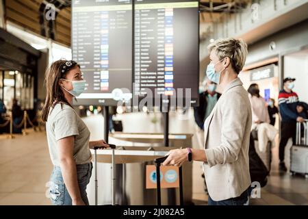 Zwei Reisende Frauen tragen Schutzmasken und diskutieren am Flughafen Faro über das Fluginformationsbrett Stockfoto