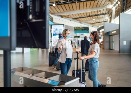 Zwei Reisende Frauen tragen Schutzmasken und diskutieren am Flughafen Faro über das Fluginformationsbrett Stockfoto