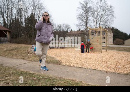 17. März 2022, Baden-Württemberg, Meßstetten: Eine aus Kiew geflohene Frau telefoniert in der ehemaligen Zollernalb-Kaserne mit ihrem Mann in der Ukraine, während ihr vierjähriger Sohn im Hintergrund mit seinem verwandten Kind spielt. In den letzten Tagen wurde in der ehemaligen staatlichen Erstaufnahmeeinrichtung im Bezirk Zollernalb ein Ankunftszentrum für Flüchtlinge aus der Ukraine eingerichtet., Foto: Marijan Murat/dpa Stockfoto