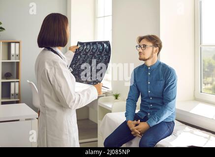 Medizinische Fachärztin, die sich ein Röntgenbild ansieht, während sie mit ihrer jungen Patientin spricht Stockfoto