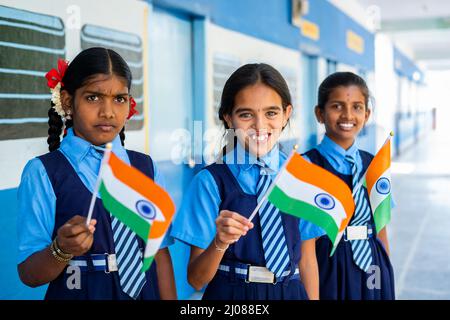 Lächelndes Mädchen kis in unifrom winkt indischen Falg durch Blick auf die Kamera auf Schulkorridor - Konzept des Patriotismus, republik oder Unabhängigkeitstag Stockfoto