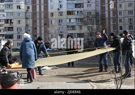 Kunststofffolien werden an die Bewohner verteilt, um defekte Fenster zu reparieren. Nachbarn und Freiwillige helfen bei der Reinigung von Trümmern und Glasscherben, nachdem ein Raketenangriff auf ein Wohngebiet in Kiew am Morgen des 17.. März 2022 Wohngebäude und ein örtliches Gymnasium beschädigt hatte. Kiew, Ukraine. Russische Streitkräfte betraten am 24. Februar 2022 das Territorium der Ukraine. (Foto von Justin Yau/ Sipa USA) Stockfoto