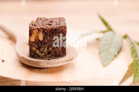 Stück Brownie mit Marihuana, auf Holzlöffel und grünem Cannabisblatt Stockfoto
