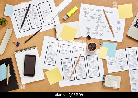 Draufsicht auf den Arbeitsbereich der vielbeschäftigten Web UX Designer mit vielen mobilen App-Wireframe-Skizzen und Benutzerablauf. Stockfoto