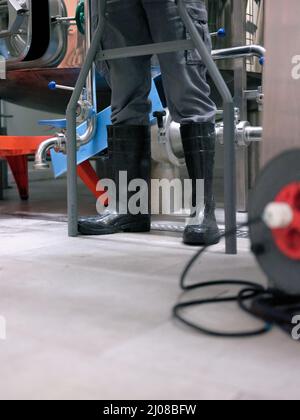 Anonymer Arbeiter mit schützenden Gummistiefeln in einer Brauerei Stockfoto