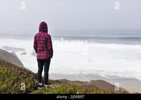 Eine Frau, die am Rand einer Klippe am Meer steht. Stockfoto