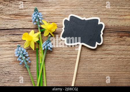 Narzissen, Muscari-Blüten und leere Tafel auf Holz. Grafikressourcen Stockfoto