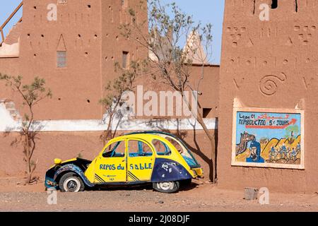 Schild an traditionellem Schlammhaus im Süden Marokkos in der Nähe eines alten Autowracks, das Tage mit dem Kamel nach Timbuktu, durch die Sahara-Wüste im Zentrum Marokkos, zeigt Stockfoto