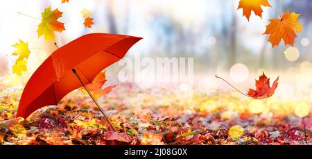 Herbsthintergrund mit rotem Regenschirm und gefallenen Ahornblättern Stockfoto