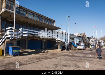 Eine Frau, die ihren Hund am Bootshaus der King's College School am Putney Embankment, Putney, London, England, Großbritannien, vorbeiführt Stockfoto