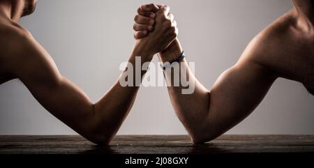 Stark muskulös bärtiger Mann, der einen schwach schwachen Mann am Arm kämpft. Arme ringen dünne Hand, großer starker Arm im Studio. Zwei Männerhände umklammten Arm-Wrestling Stockfoto