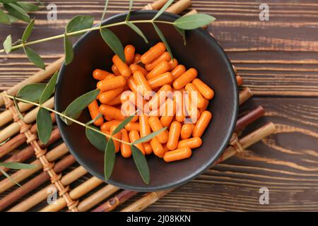 Schale mit Kurkuma-Pulverkapseln auf Holzgrund Stockfoto
