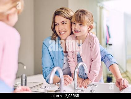 Drinnen kann es Spaß machen. Aufnahme einer fröhlichen jungen Mutter und ihrer Tochter, die sich die Hände waschen, während sie ihre Spiegelung in einem Spiegel betrachten. Stockfoto