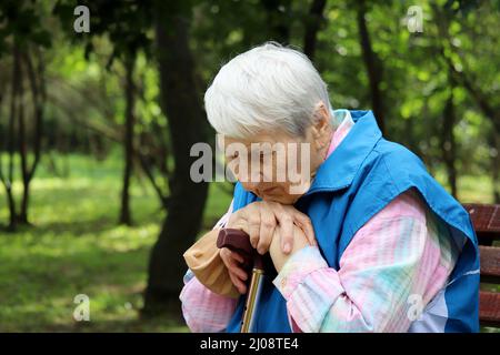 Porträt einer älteren grauhaarigen Frau, die mit Gehstöcken auf einer Bank in einem Park sitzt. Gesunde Lebensweise im Alter, Leben im Ruhestand Stockfoto