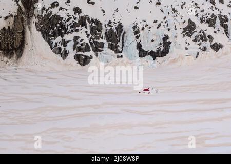 Das Winter-Biwak aus acht Zelten, die auf dem Glacier d'Argentiere vor einer Kulisse aus eisbedeckten Klippen aufgestellt wurden, wobei der Schnee teilweise von rotem Sand bedeckt war Stockfoto