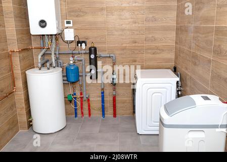 Ein moderner Gaskessel-Raum mit Keramikfliesen, die Holz imitieren, sichtbarer kompletter Heizraum-Ausstattung mit Waschmaschine und Wasserenthärter. Stockfoto