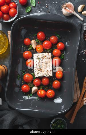Vorbereitung von Fetapasta. Feta-Käse und Tomaten in einer Auflaufform auf schwarzem Hintergrund. Draufsicht. Stockfoto