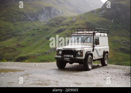 Weißes Land Rover Defender 90 4x4-Fahrzeug, geparkt bei der A82 in Glencoe mit dem Hidden Valley und dem Berg Bidean nam Bian im Hintergrund. Stockfoto