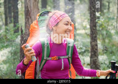 Ein weiblicher Wanderer sprüht ein Aerosol, um sich vor blutsaugenden Insekten und Zecken, Trägern gefährlicher Krankheiten und Parasiten, zu schützen. Auf dem Weg in der Stockfoto