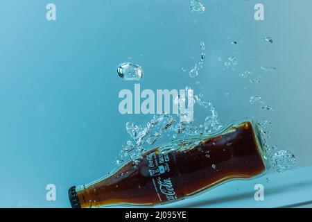 Nahaufnahme einer Flasche Coca-Cola, die auf blauem Hintergrund in die Wasserisolation fällt. Schweden. Uppsals. Stockfoto