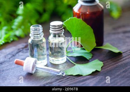 Pipettenflasche, Tinktur und Ginkgo-Blätter auf Holzhintergrund verziert. Homöopathisches Konzept. Stockfoto