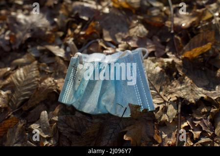 Nahaufnahme einer lichtdurchfluteten Gesichtsmaske in hellblau achtlos auf dem Waldboden weggeworfen Stockfoto