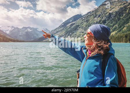 Wandermädchen, die auf ein Wahrzeichen zeigt und auf einem hölzernen Pier für Fischerboote auf einem malerischen Bergsee steht Stockfoto