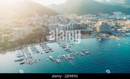 Luftaufnahme von oben nach unten von Bootsanlegestelle und Yachthafen in Budva, Montenegro. Weiße private Motorboote werden an der adriatischen Küste an der Anlegestelle vertäut. Yachtclub Stockfoto