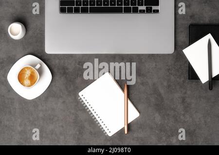 Arbeitsbereich von oben mit Laptop, Notizblock, Stiften und Kaffee auf dunkelgrauem Steinhintergrund. Flach liegend mit Kopierplatz. Geschäftskonzept. Stockfoto