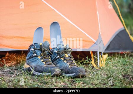 Ein Paar nasse und schmutzige Wanderschuhe trocknen in der Nähe des Zeltes, wobei die Innensohle heraussteht Stockfoto