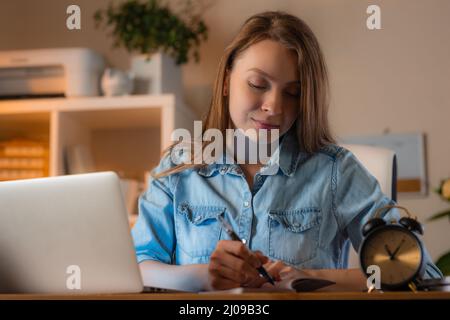 Schöne lächelnde Frau, die an ihrem Arbeitsplatz im Büro arbeitet, einen Laptop benutzt und Notizen macht. Konzept für schöne Arbeit. Stockfoto