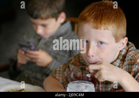 Kinder sehen sich in derselben Familie beim Familientreffen Computerspiele an, bei denen beide Gesichter dabei zusehen, wie die Cousins der Spiele Spaß haben Stockfoto