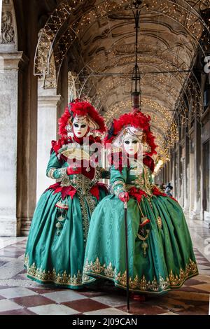 Vertikale Aufnahme von zwei Frauen in Karnevalskleidung und Masken, die auf einer gewölbten Terrasse stehen Stockfoto