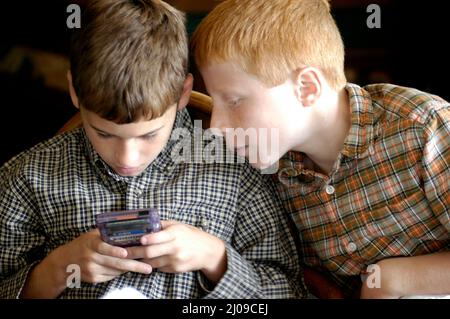 Kinder sehen sich in derselben Familie beim Familientreffen Computerspiele an, bei denen beide Gesichter dabei zusehen, wie die Cousins der Spiele Spaß haben Stockfoto