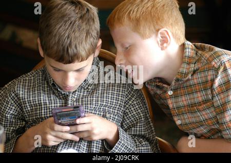 Kinder sehen sich in derselben Familie beim Familientreffen Computerspiele an, bei denen beide Gesichter dabei zusehen, wie die Cousins der Spiele Spaß haben Stockfoto