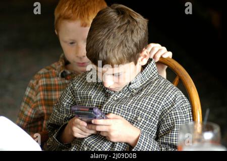 Kinder sehen sich in derselben Familie beim Familientreffen Computerspiele an, bei denen beide Gesichter dabei zusehen, wie die Cousins der Spiele Spaß haben Stockfoto