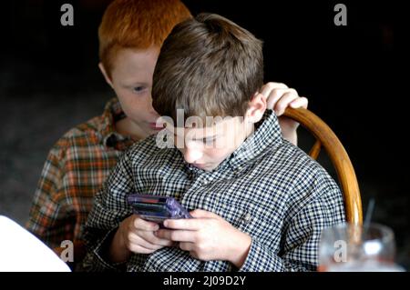 Kinder sehen sich in derselben Familie beim Familientreffen Computerspiele an, bei denen beide Gesichter dabei zusehen, wie die Cousins der Spiele Spaß haben Stockfoto