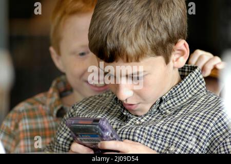 Kinder sehen sich in derselben Familie beim Familientreffen Computerspiele an, bei denen beide Gesichter dabei zusehen, wie die Cousins der Spiele Spaß haben Stockfoto