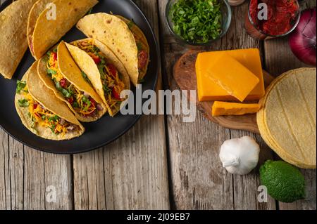 Draufsicht auf Teller mit leckeren mexikanischen Tacos auf rustikalem Holztisch mit Zutaten für das Kochen Hintergrund. Konzept der traditionellen Mahlzeit. Appetitliches Pho Stockfoto