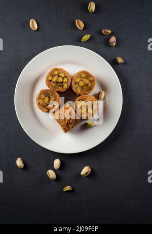 Traditionelle arabische Süßigkeit - Baklava. Türkisches Dessert oder Süßes auf einem weißen Teller serviert, von oben vor schwarzem Hintergrund geschossen. Stockfoto