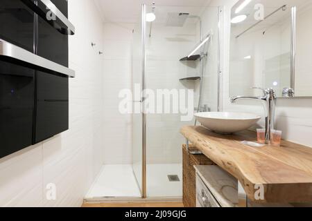 Toilette mit Waschbecken in weißer Schale auf Holzkäfelarbeitsplatte und Duschkabine mit Glasabtrennung Stockfoto