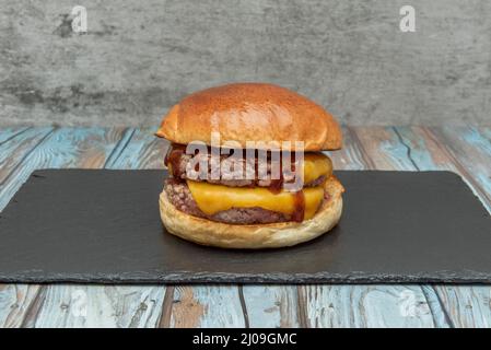 Der doppelte Cheeseburger mit zwei Fleischstücken, gewürzt mit einem Schuss Salz und Pfeffer Ketchup und Cheddar-Käse auf einem Holzbrett auf einem blauen Holzbrett Stockfoto