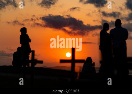 Silhouette von Menschen und Kreuzen, die auf dem Boden zu Ehren der von Covid-19 Getöteten befestigt sind. Sonnenuntergang in Salva Stockfoto