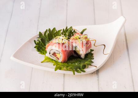 Uramaki-Rolle in roten Thunfisch verpackt, ergänzt mit Frischkäse und einer speziellen Sauce auf Shiso-Blättern Stockfoto