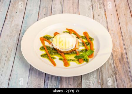 gemüsetartine mit Ziegenkäse, Karottencreme, Pesto-Sauce und Olivenöl auf einem weißen Teller Stockfoto