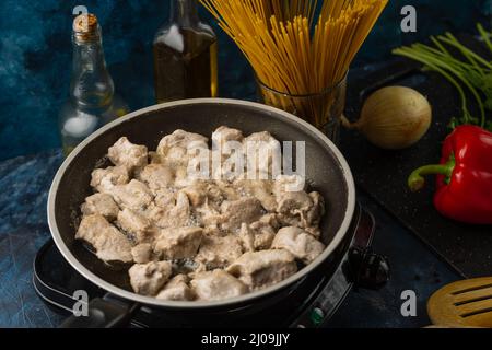 Makroaufnahme der Bratpfanne mit duftendem gegrilltem Fleisch auf dem Herd auf Zutaten zum Kochen Hintergrund. Lebensmittelkonzept. Hausgemachte Mahlzeit. Traditionell Stockfoto